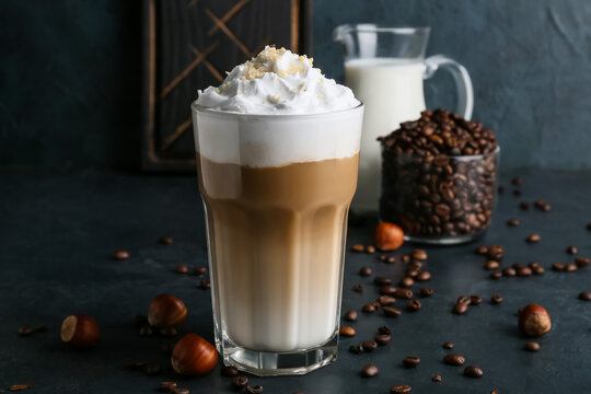 Glass of tasty latte with nuts and coffee beans on black background