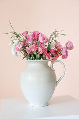 Bouquet with eustoma, summer flowers in a white vase, on a pink-beige background.