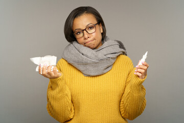 Unhealthy young woman with runny nose or sinusitis holding nasal drops and tissues. Unhappy black...