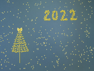 Christmas tree lined with dry pasta and numbers 2022 and stars from pasta on a blue paper background.