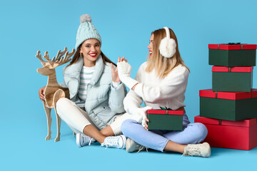 Young sisters with Christmas gifts giving each other high-five on blue background