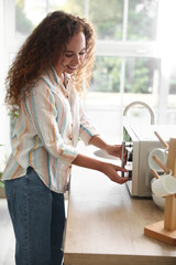 Young African-American woman adjusting microwave oven in kitchen