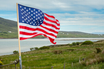 Flag of United States of America waving in a wind. Green mountains in the background. USA symbol in nature environment. Rural area with green field and ocean in the background