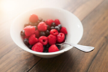 Raspberry and blueberry in a white bowl on a wooden table. Healthy fruit mix. Produce product. Healthy diet choice.