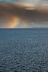 Colorful rainbow symbol of luck over rich blue water surface. Dark dramatic sky. Copy space. Nature wonder. Nobody