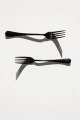 Two forks with sharp shadows of sun on a white background. Menu design concept. Flat lay. Copy space.