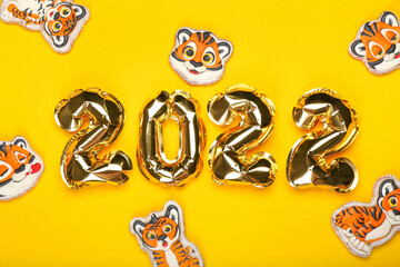 Balloons in shape of figure 2022 and tiger cookies on color background