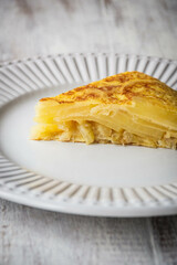 Porción de tortilla española en un plato blanco sobre una mesa de madera blanca rústica