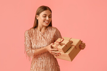 Beautiful young woman with Christmas gifts on pink background