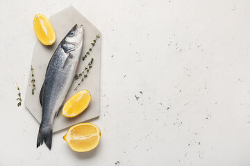 Board with fresh uncooked sea bass fish and lemon on white background