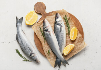Wooden board with fresh uncooked sea bass fish on white background