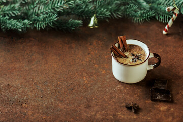 Obraz na płótnie Canvas A mug of hot chocolate or cocoa with cinnamon sticks and pieces of chocolate on the background of fir branches.Christmas and winter holidays.Glass of winter drink on rusty background with copy space 
