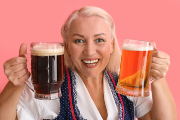 Adorable Oktoberfest woman holding mugs with beer on pink background