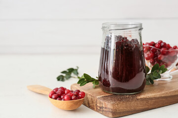 Jar with tasty lingonberry jam and fresh berries on table
