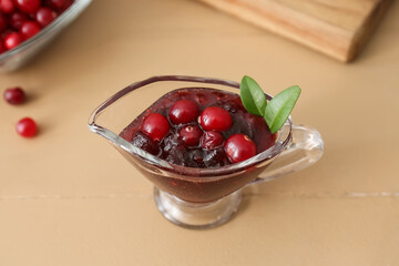 Gravy boat with tasty lingonberry jam on beige wooden background