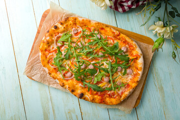 Roman pizza, Pinsa with sausages and arugula on roman dough isolated on mint wooden table top view