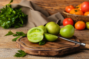Board with green tomatoes and knife on wooden background
