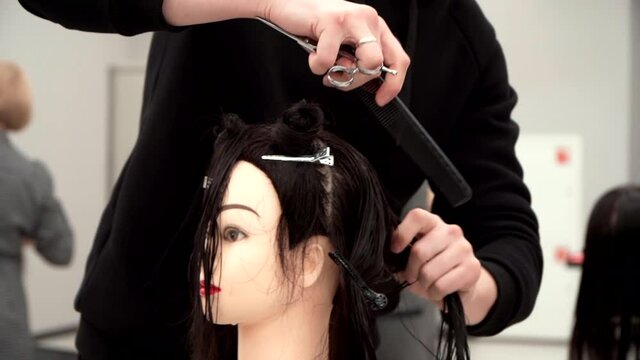Caucasian guy in black clothes cuts the mannequin's hair