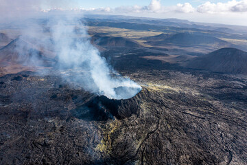 Fototapeta na wymiar Aerial drone view of Fagradsfjall volcano in Iceland. Smoke is spewing out of volcano, black lava landscape.