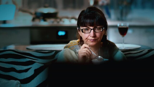cinematic woman watching tv at home in the evening and eating ice cream, good mood