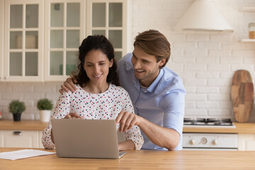 Obraz premium Attractive young couple look at laptop discuss purchase, choose e-services, buy goods, make food order on-line. Satisfied clients of electronic commerce services, modern tech for comfort life concept