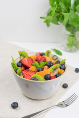 Fresh, healthy chopped fruit salad in a bowl on white  background. Top view. Strawberry, blueberry, kiwi, orange, mint..