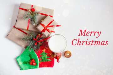 Merry Christmas Greeting card, frame. Winter holiday concept. Red ribbon, Handmade gift boxes, milk, cookies, protective masks with Ilex, Holly and Xmas decoration on white background top view banner  - Powered by Adobe