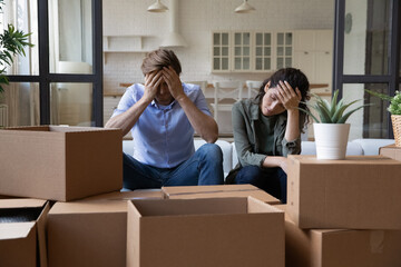 Exhausted young couple sit rest on sofa in living room near heap of cardboard boxes feel...