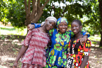 Three radiant young African women in beautiful traditional dresses looking at the camera; human...