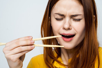 woman eating sushi with japanese chopsticks posing light background