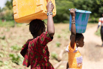 Two young black African girls who are transporting water cans instead of going to school; child...