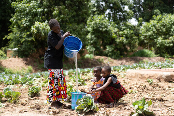 Two little black girls and a young teenage girl help water their family's garden