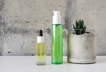 Natural cosmetic facial skin care set and a succulent in concrete pot on white desk on cement wall background. Beauty products template for branding. Serum and cleaner bottles