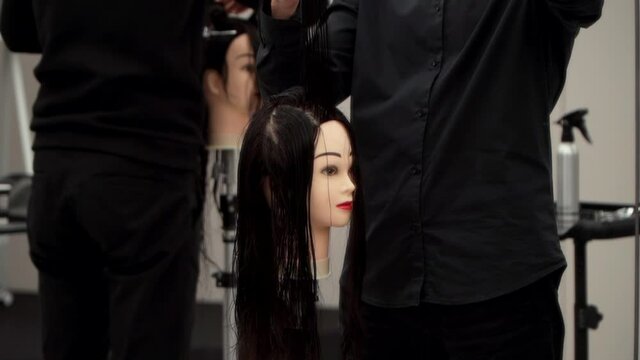 Caucasian guy in black clothes cuts the mannequin's hair