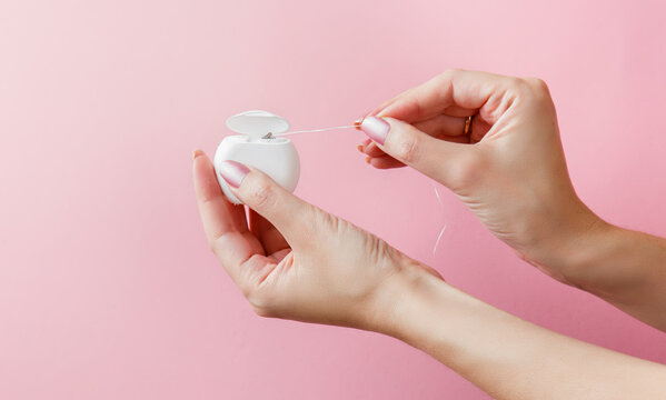 dental floss in female hands on pink background. Care of teeth health. Everyday routine teeth cleaning and flossing. Woman hands holding dental floss, close up