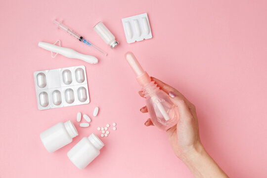 vaginal enema in woman hand, suppositories, tablets, applicator on pink background, treatment of vaginal infections from candidiasis, thrush, sexually transmitted infections. Female health. Top view