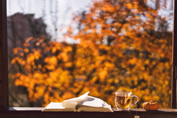 Naklejka na ściany i meble A cup of hot tea and open book on a vintage windowsill. Still life details in home on a wooden window. Read and rest. Cozy autumn concept.