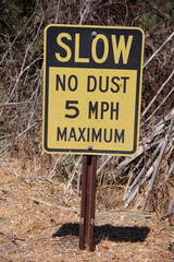 A road sign SLOW NO DUST 5 MPH MAXIMUM on a rural dirt road through vineyards