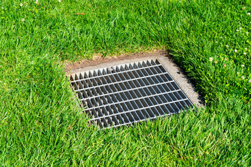 Catch basin square drainage grate over storm water drain surrounded by green grass.