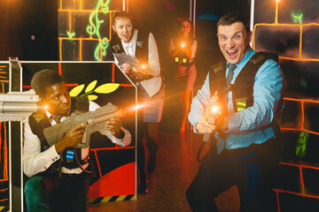 Emotional portrait of adult men and women co-workers having corporate entertainment in laser tag room