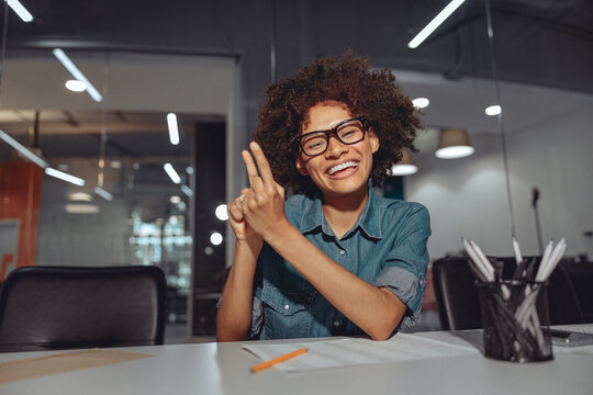 Smiling African American lady talking with sign language while sitting at her workplace in the office