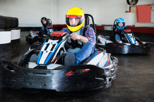adult man in helmet and other people driving car for karting in sport club indoor