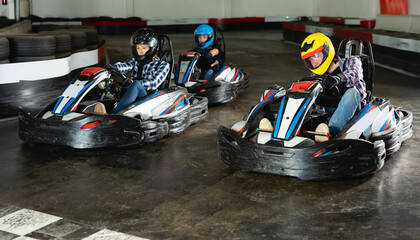 Group of happy male and females in helmets driving racing cars at kart track