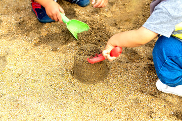 砂遊びに夢中の2人の子供達　黄緑と赤のスコップで砂遊び