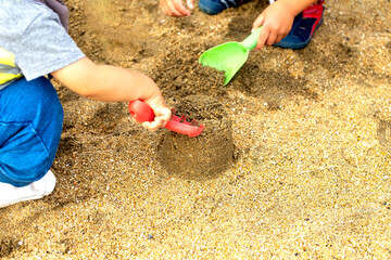 砂遊びに夢中の2人の子供達　黄緑と赤のスコップで砂遊び