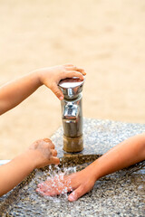 公園の水飲み場で水遊びする子供達2人の手。または手を洗おうとしている子供達の手