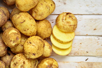 Heap of natural yellow fresh tuber of potatoes and cutting chips on wooden plank. Top view