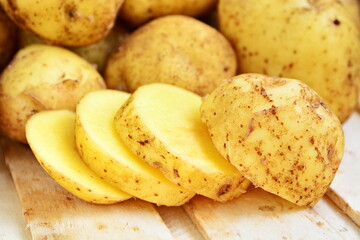 Heap of natural yellow fresh tuber of potatoes and cutting chips close up on wooden plank