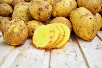 Heap of natural yellow fresh tuber of potatoes and cutting chips on wooden plank