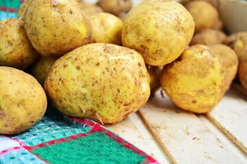Vegetables in wooden box. Heap of natural yellow fresh tuber of potatoes close up on a checkered...